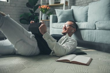 Kanepeye uzanıp tabletini kullanarak sohbet eden bir adam. Evde, tablet kullanıyor, izliyor, komik filmleri tartışıyor, çevrimiçi diziler, konuşmalar...