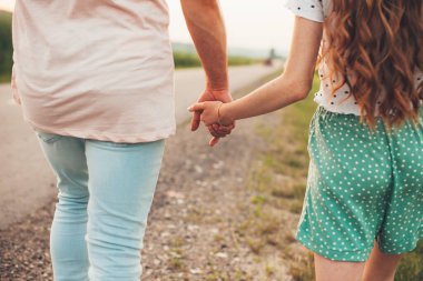 İlkbahar doğasında, şehir dışında kırsal yolda yürürken sevgi dolu bir çiftin el ele tutuşması. Yaz tatili kavramı. Romantik çift randevusu. Aşk