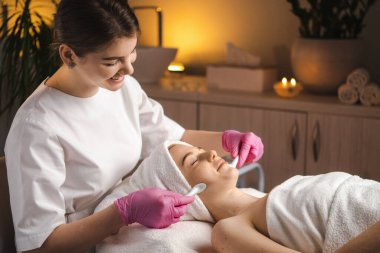 Beautician making skincare and stimulation facial procedure to a patient in the spa salon. Facial treatment. Cosmetology concept.