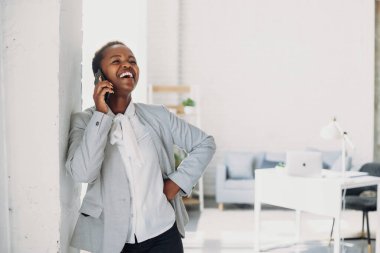 Afro woman entrepreneur smiling while talking on mobile phone standing in the office. Modern communication. Modern technology.