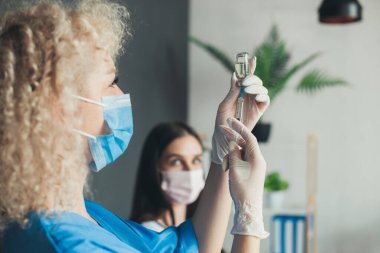 Female doctor extracting a covid-19 vaccine injection with a syringe needle, wearing surgical protective mask. Coronavirus vaccination. Pandemic prevention