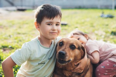 Cute boy and baby girl sitting on the grass with their dog in the backyard. Portrait for game design. Summer vacation fun. Summer nature.