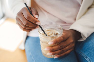Close-up view of African womans hands mixing the drink with the straw before drinking it. Lifestyle concept