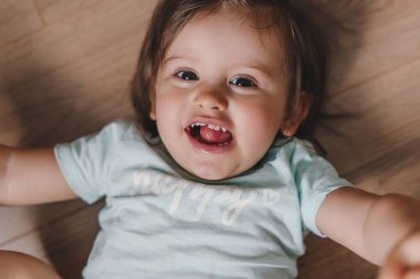 Closeup portrait of a baby girl lying on her back on the wooden floor. Skin care. Childhood concept. Smiling happy child. Baby development. Happy family