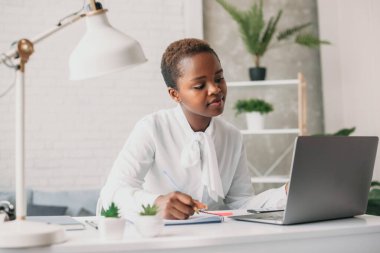 Black woman student studying foreign language at home, looking webinar on laptop. Remote work concept. Usage of modern technologies. Chatting with friend