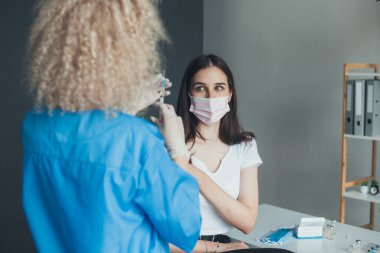 Curly-haired doctor administrating COVID-19 Vaccine to a patient at the hospital. Pandemic prevention. Coronavirus vaccination.