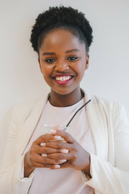 Portrait of a smiling african american woman holding a glass an looking at camera isolated over white wall. Beautiful girl portrait. Beautiful black woman.