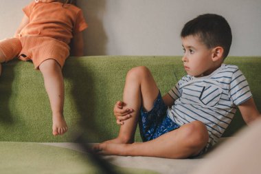 Sister and brother spending time in the afternoon sitting on the couch. Happy children spending free time, weekends or evening in cozy room.