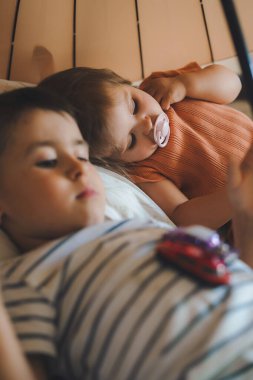 Lovely baby girl with her brother lying down on the floor under an umbrella, indoors. Education concept. Home concept. Health insurance concept.