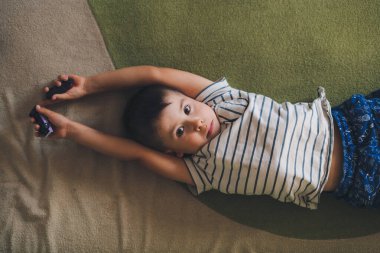 Top view of a boy lying on his back on the bed looking sleepily into the camera. Expression on his face. People, youth and lifestyle concept.