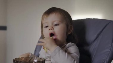 Baby girl having breakfast in her baby seat. Holding cake dessert. Face and mouth smeared, smeared with cream.