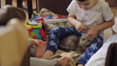 Little girl and boy in pajamas playing with cute pet animal at home, sitting on bed. Happy time together with friend pet. Excited Smiling boy Enjoying With His