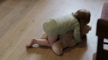 View from top, of a baby girl lying and holding a teddy bear, playing on the floor. Beautiful girl portrait. Cute teddy bear toy.