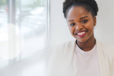 Afro woman in white jacket posing smiling at camera standing in the office. Successful and confident. Close up portrait.
