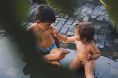 Two cute kids sitting in the yard of their house and playing with water. Spring, summer garden. Summer nature. Summer vacation fun.