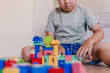 Caucasian boy sitting at home on the floor and playing with wooden brick blocks toys. Kid play with educational toys at kindergarten.nThe creative playing of