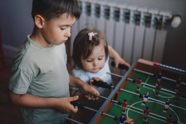 Big brother spending playtime with his younger sister playing foosball together. Sports football game. Happy family.