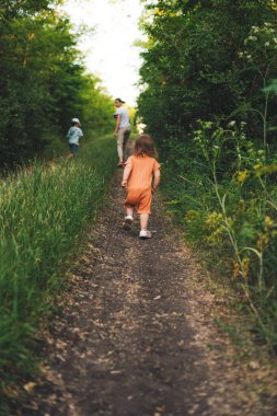 Family of three walking down the road. Happy family outdoors. Back view. Green grass field. Active travel.