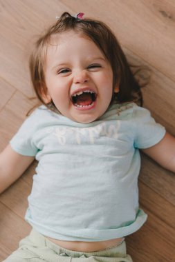 Laughing girl lying on the floor on her back and looking directly into the camera. Smiling happy child. Positive person. Beauty portrait. Smiley face.