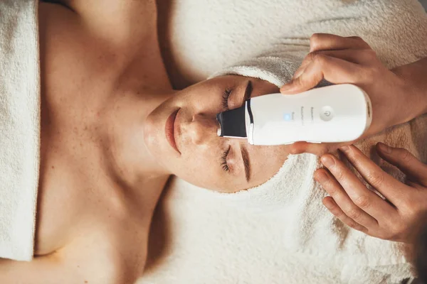 Top view of relaxed womans face getting ultrasound facial cleaning in spa salon. Happy face. Body care.