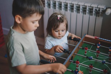 Portrait of brother with his little sister playing table football at home. Children play table games. Happy family.