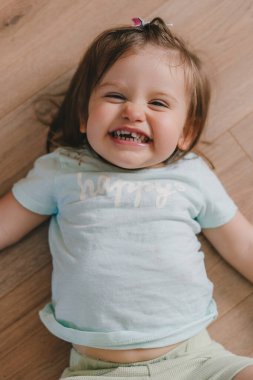 Top view portrait of a cute baby girl lying on his back on the wooden floor, smiling at camera. Concept of a happy childhood. Child care.