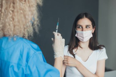 Nurse administrating the coronavirus vaccine to a woman patient with face mask at hospital. Virus, epidemic, disease. Coronavirus vaccination.