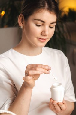 Portrait of a beautician collecting the cream with a spatula from a jar, ready to apply it on womans face. Testing and advertising of products, care cosmetics.