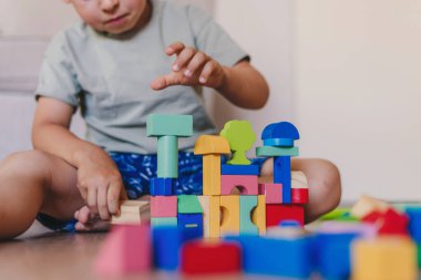 Caucasian boy playing with wooden blocks at home. Childcare concept. Child playing with cubes on the floor