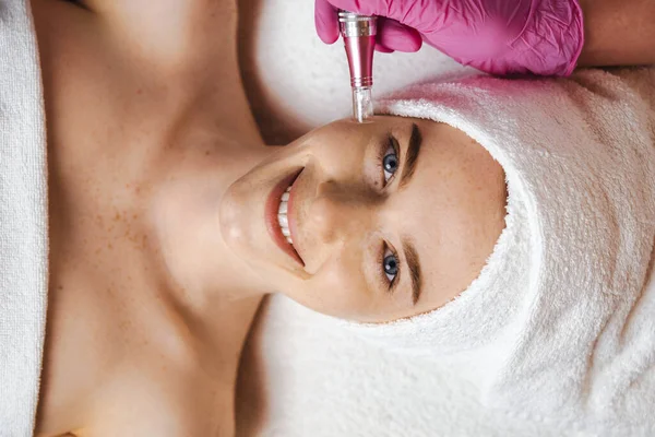 Smiling freckled woman patient receiving procedure Microdermabrasion of the facial skin in a beauty salon. Professional beauty salon. Woman beauty face. Skin