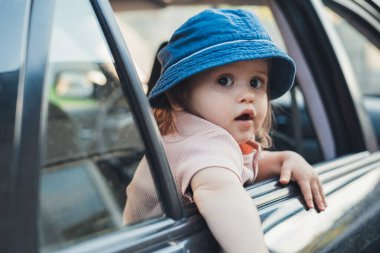 Baby girl sticking his head out of a car window, looking back to the camera. Cars heading forward to travel to natural places.
