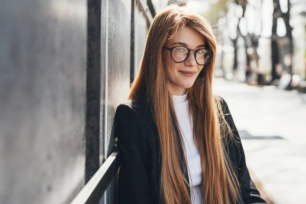 Portrait of a successful woman looking straight into the camera smiling, wearing glasses. Beautiful girl portrait. City lifestyle. Travel fashion. Female
