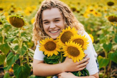 Happy farmer woman hugging some sunflower flowers, enjoying a rich harvest. Natural beauty. Summer nature. Smiling girl.