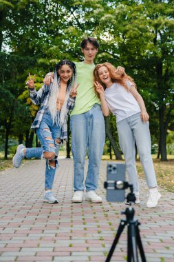 Three teenagers of different nationalities posing in the park to post a story on social network. Popular bloggers. Standing outside at a park.