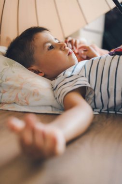 Adorable boy lying on his back on the playroom floor under the umbrella with his sister to put her to sleep. People lifestyle concept. Childhood concept. Health