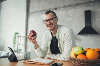 Man using tablet in kitchen to watch movie while taking a short break from studying to eat an apple. Watching movie or program. Remote work or out of office