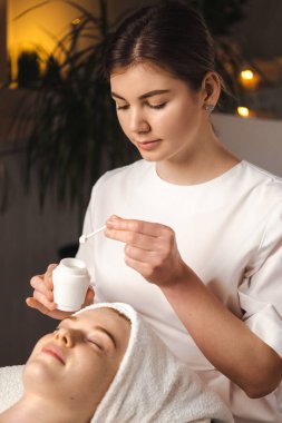 Beautician holding a jar of face cream wanting to apply on the patients face. Dermatology, cosmetology. Skin treatment. Beauty portrait.