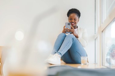 African-american woman checking her news feed, enjoying tasty fresh drink at coffee shop, using high speed internet connection. Connected to wireless internet