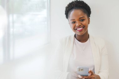 Smiling African American businesswoman surfing internet on mobile phone, reading news, sitting at cafe in the morning. Healthy breakfast. Healthy drink. Healthy