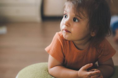 Baby girl leaning on the sofa and looking focused on what is going to be shown on the TV. Relaxing on the weekend. New lifestyle after covid
