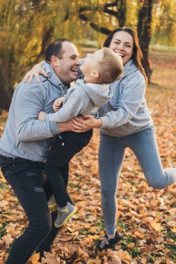 Happy family of three members resting in autumn city park posing against the beautiful yellow trees. Happy family outdoors. Activity relationship. Parent, child