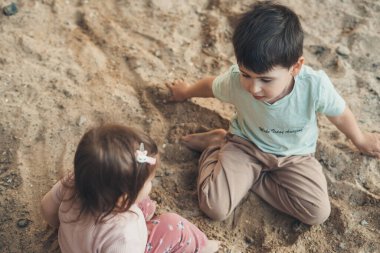 Two kids playing, sitting on the sand spending time in games, having fun together. Brother and baby sister. Summer activities.