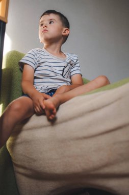 Caucasian boy sitting alone with thinking face, looking out. Space for text. International Childrens Day. Looking away from camera