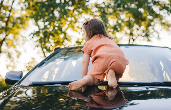 Baby crawling on all fours on the hood of her fathers car. Active kid playing outdoors. Happy family, childhood.