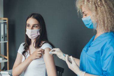Young female nurse in medical face mask and gloves holding syringe and giving female patient flu vaccine injection in arm. irus, epidemic, disease. Health care