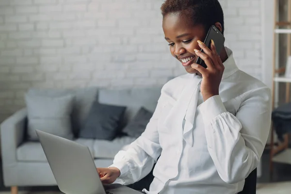 African-american entrepreneur woman with laptop talking on mobile phone smiling in office. Social networks communication, mobile connection.