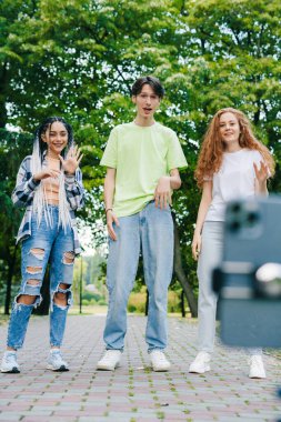 Three diverse teenagers blogger making video for internet blog outside in summer park, using gadgets. Selfie time, blogging. Selfie culture, social network