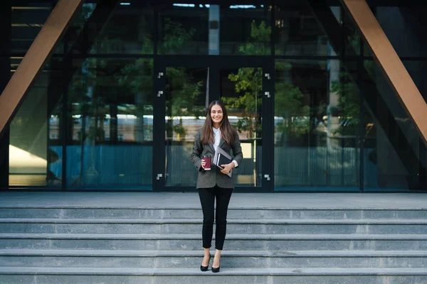 Front view of a businesswoman walking down stairs and holding laptop and drinking takeaway coffee. Business success concept. Business, lifestyle concept. People