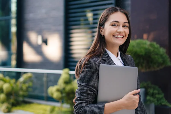 Caucasian business woman holding laptop computer, walking into office building. Outdoors. Copy space, Business concept, portrait of office. Business meeting