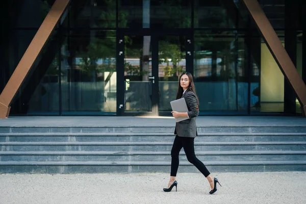 Modern businesswoman freelancer holding laptop walking into office building after the break. People urban lifestyle concept. Creative business, diversity